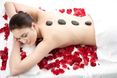 Woman lying down on rose petals with stones on back